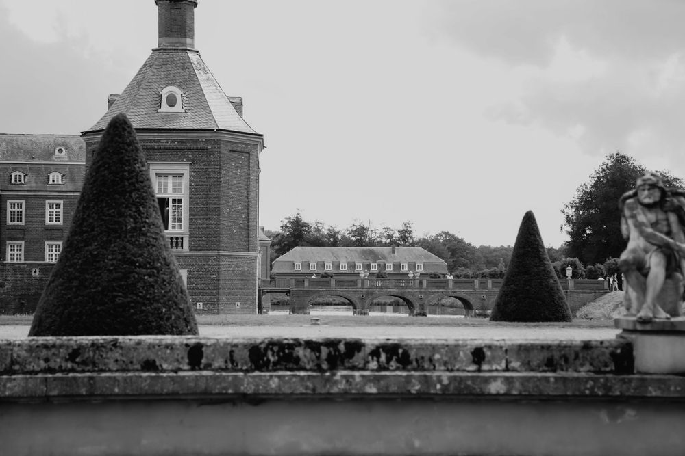 Black and white architectural photo of a grand estate with manicured topiary and decorative statues.