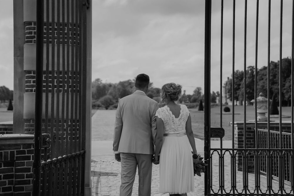 Black and white wedding photo of couple walking through ornate iron gates.