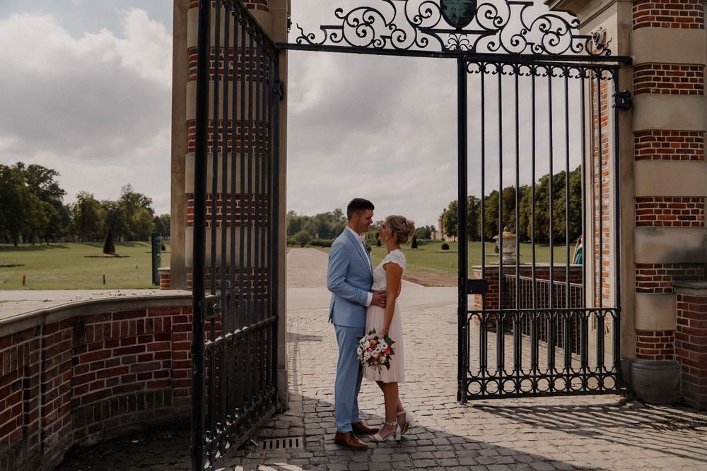 Wedding portrait at ornate gateway entrance with brick walls and garden view.