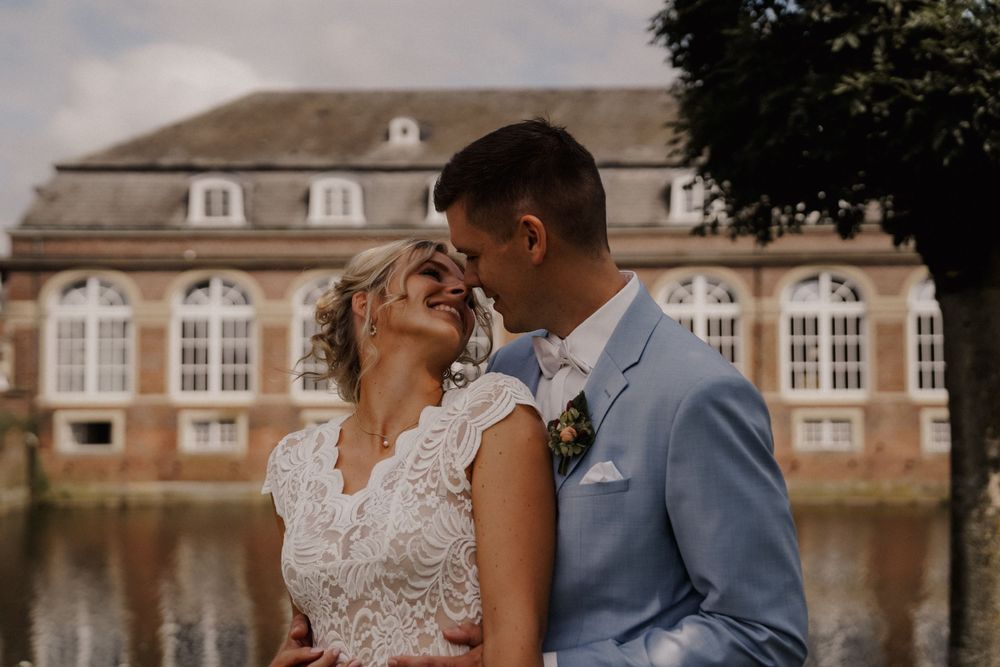 Romantic wedding portrait with historic building and water feature in background.