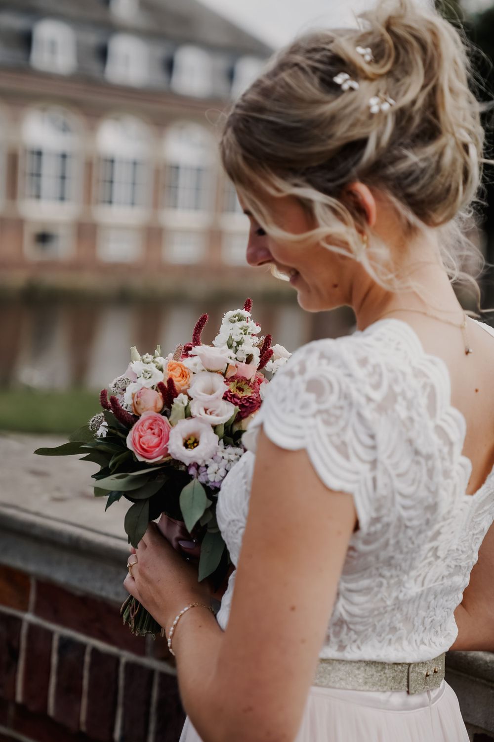 Close up of bridal bouquet with pink roses and white lace dress details.