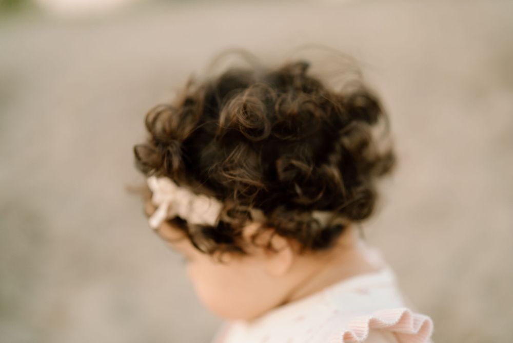 Close-up profile view of a small child with dark curly hair wearing a white top against a soft blurred background.