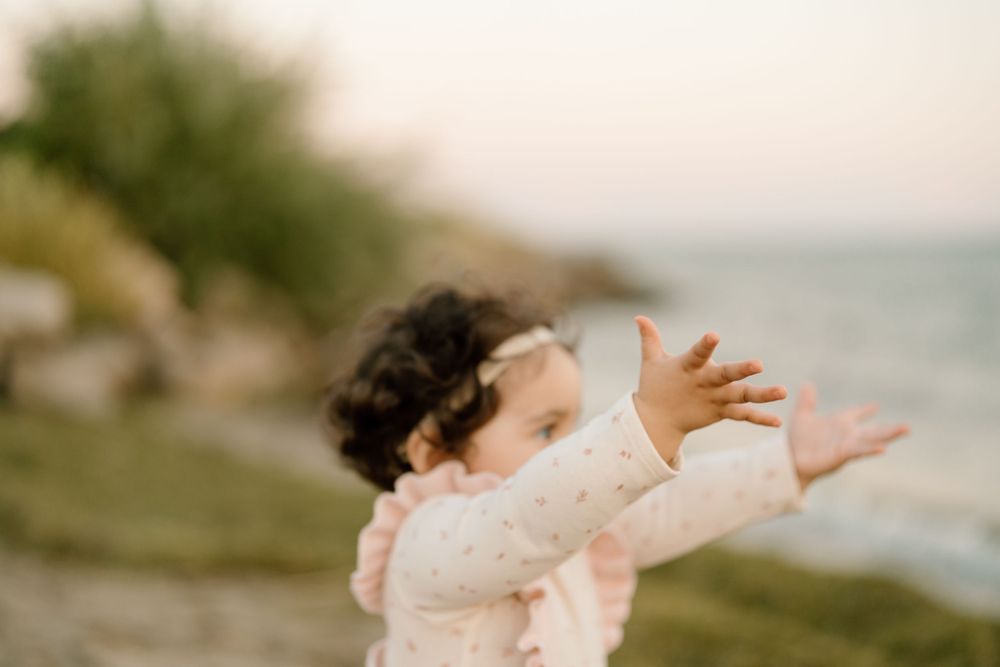 A figure in a white lace dress stands with outstretched arms against a dreamy coastal sunset background.