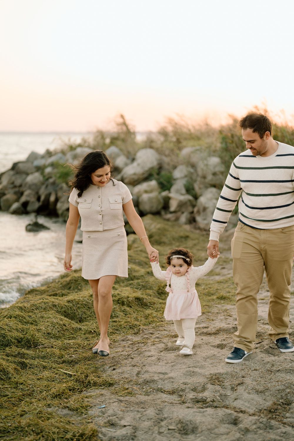 Family walking together on a beach path at sunset with rocks and ocean in the background.
