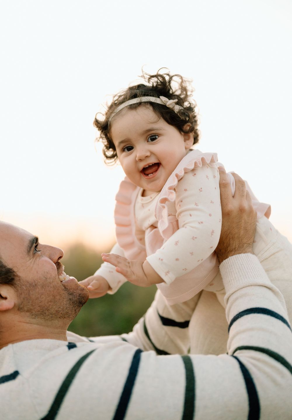 A joyful moment captured between parent and baby during sunset outdoors.
