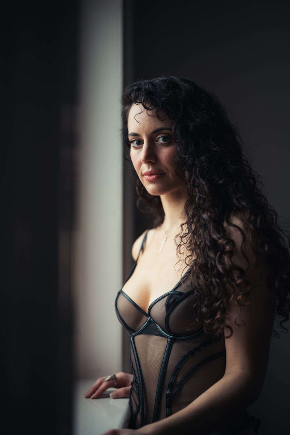 Dramatic boudoir portrait with dark lighting and curly hair against a shadowy background.