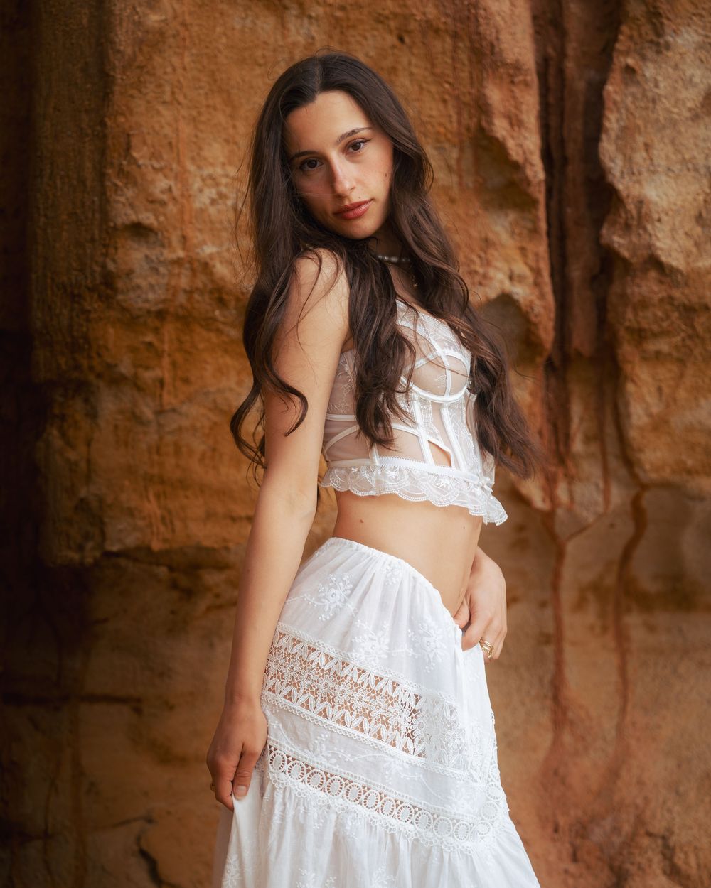 Person in white lace crop top and skirt poses against red rock formation.