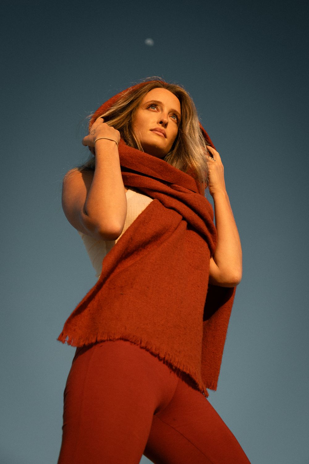 Abstract fashion portrait in rust-colored clothing against blue sky with dramatic angle.