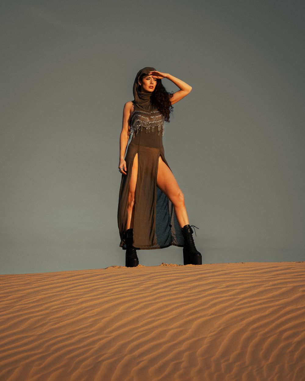 Fashion model in black dress poses dramatically on sand dunes at sunset.
