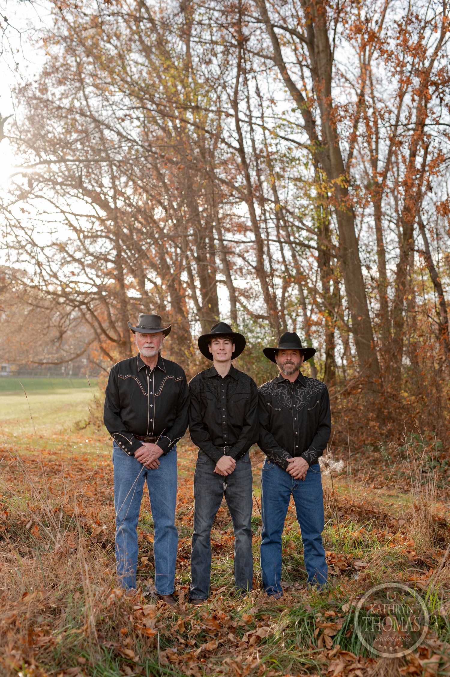 Three people in cowboy hats and western wear standing among fall trees.