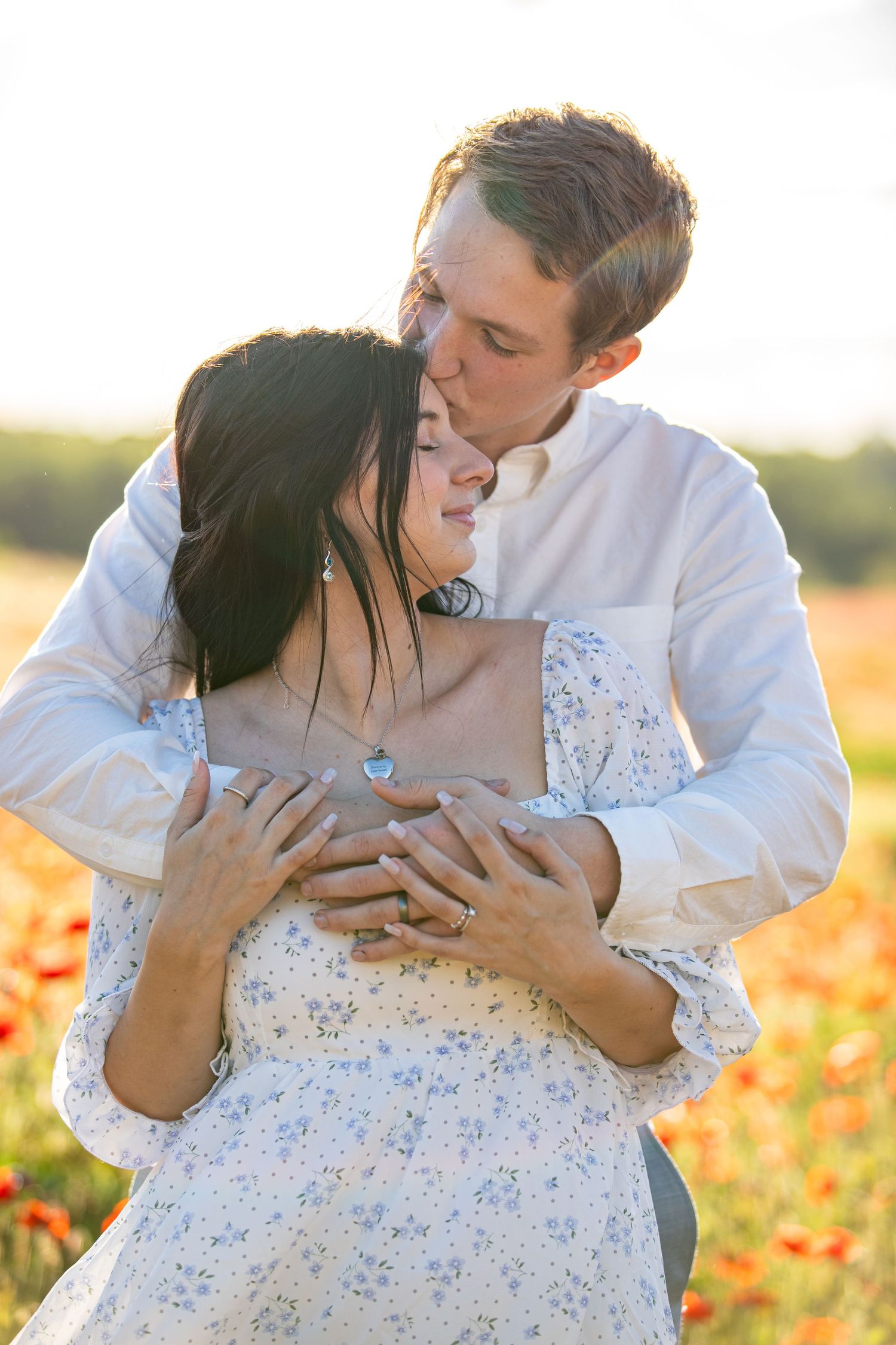 Tender embrace in a sunlit wildflower field during engagement or wedding photoshoot.