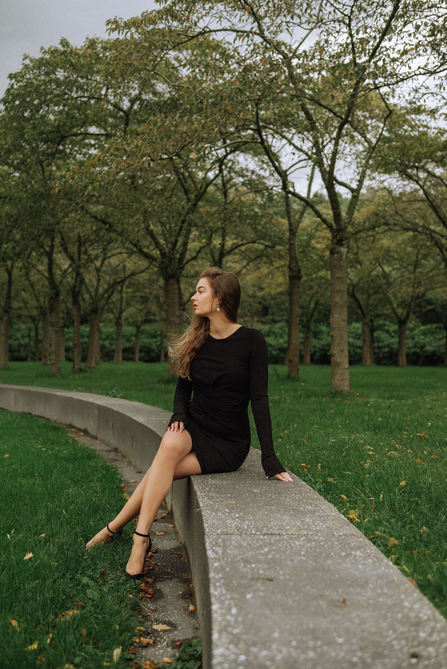 A chic solo photoshoot in Amsterdam with a stylish little black dress outfit against neatly trimmed lawns and pathways.