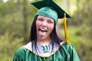 Playful graduate in green cap and gown sticking tongue out during graduation photo.