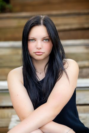 Portrait of person with long dark hair sitting on wooden steps outdoors.