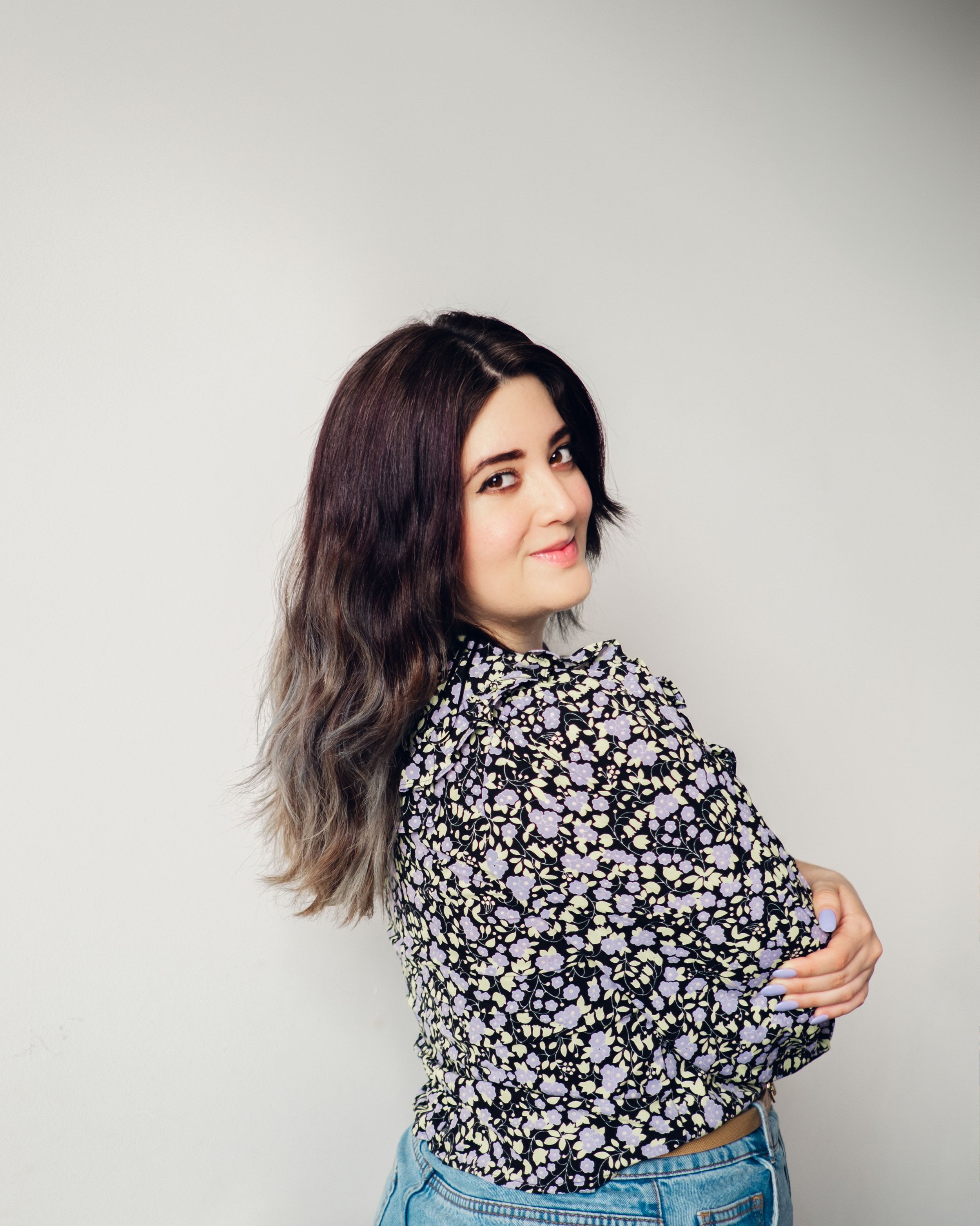 Portrait of someone in a floral print top posing against light gray background.
