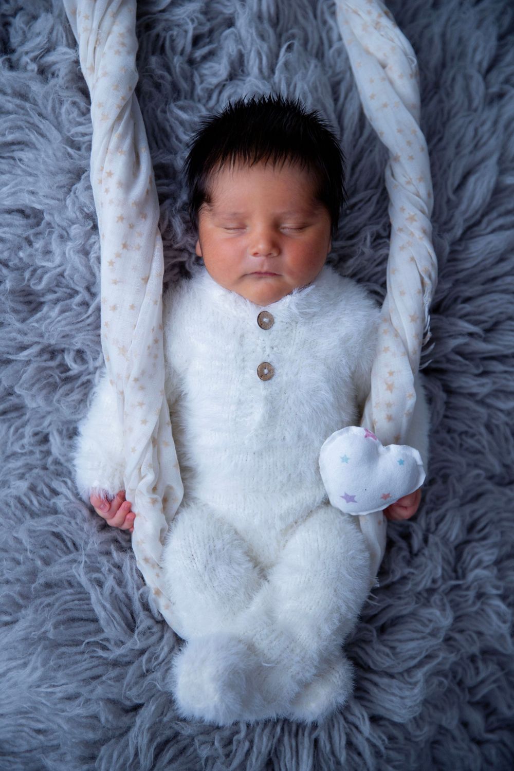 Newborn baby in soft white outfit lying on textured blanket during studio newborn photography session.