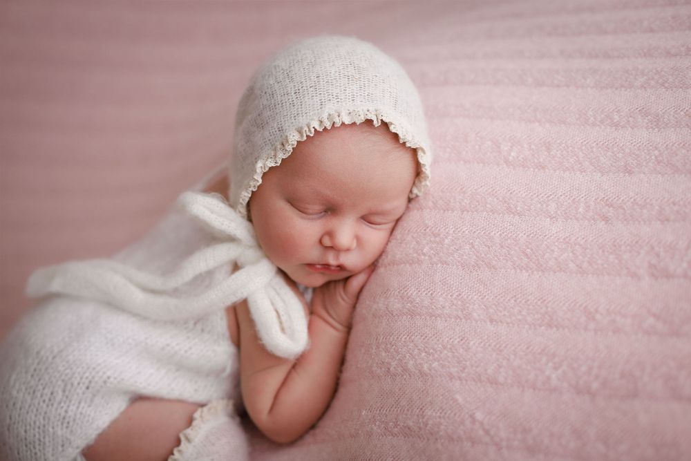 Sleeping newborn in white knit outfit on soft pink blanket during Central Florida newborn session.