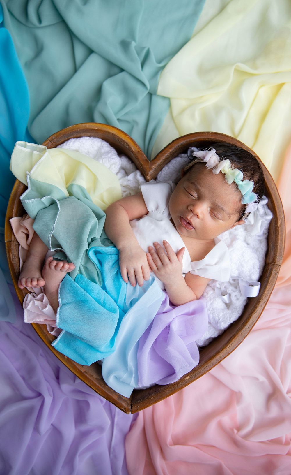 Sleeping newborn in heart-shaped prop during artistic newborn photography session in studio.