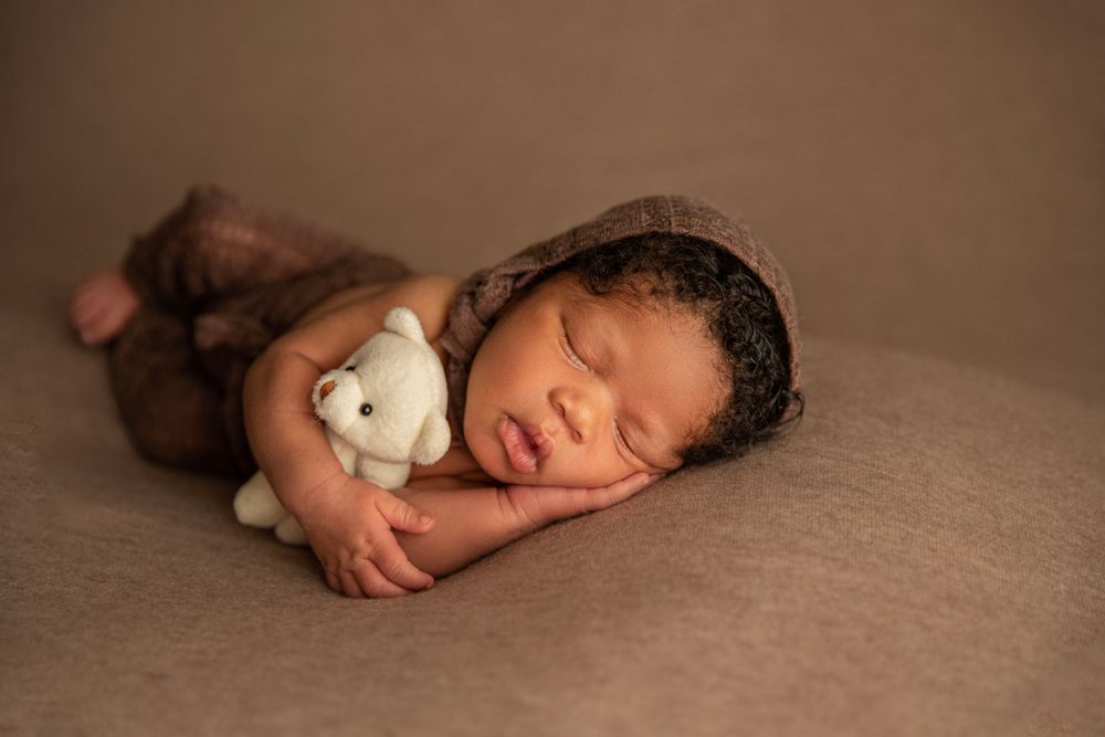 Sleeping newborn in town outfit holding teddy bear during Orange City newborn photography session.