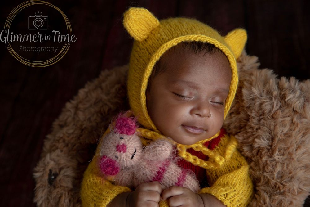 Sleeping newborn in Winnie the Pooh inspired outfit during themed newborn photography session in studio.