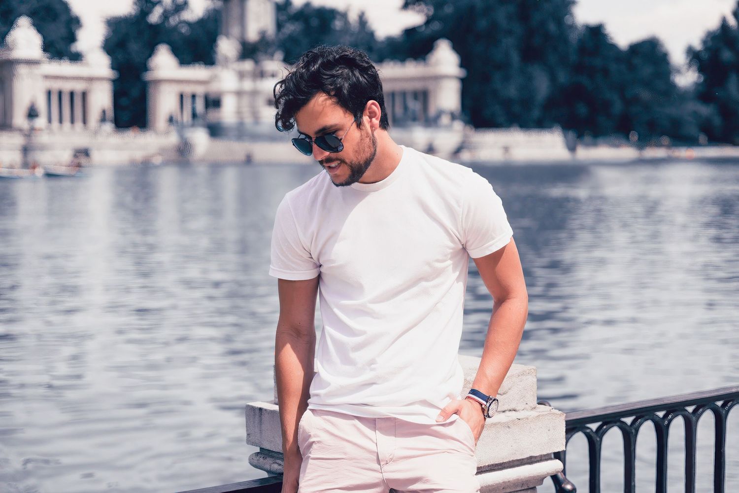 Person in white t-shirt and sunglasses standing by lakeside railing.