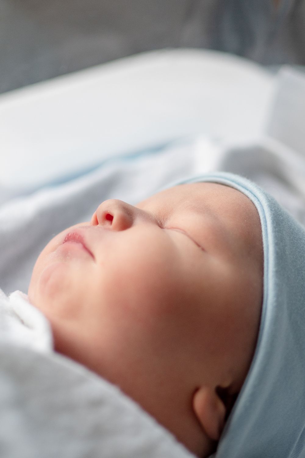 A peaceful newborn baby sleeps quietly while swaddled in soft blue and white blankets.