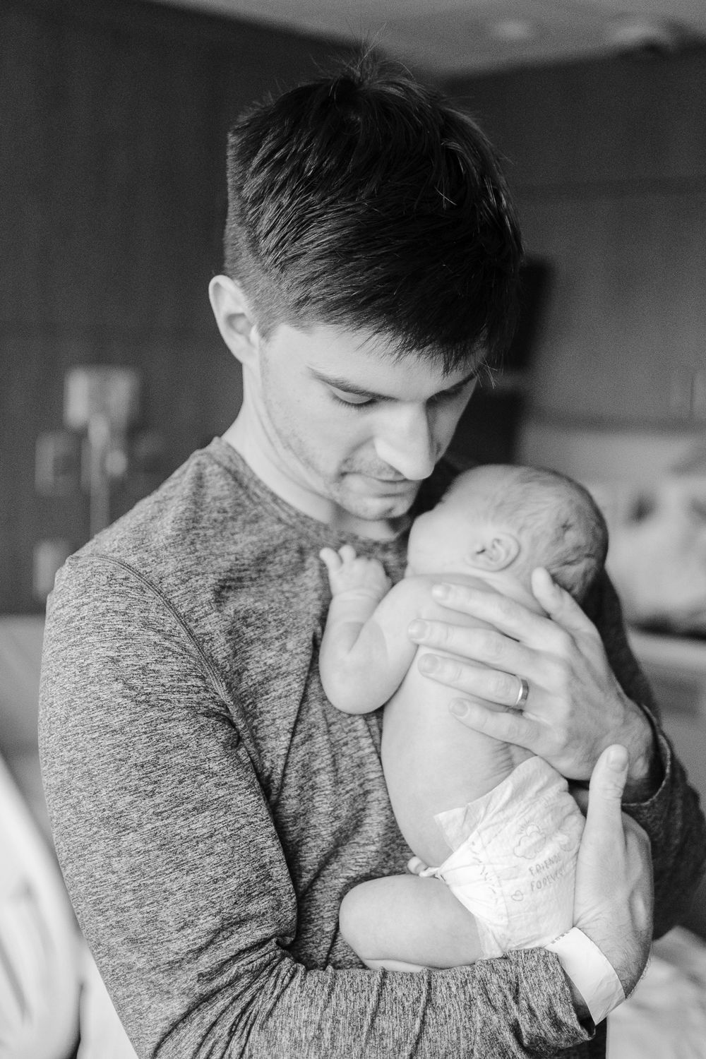 A tender black and white moment shows someone in a gray sweater cradling a sleeping newborn baby.