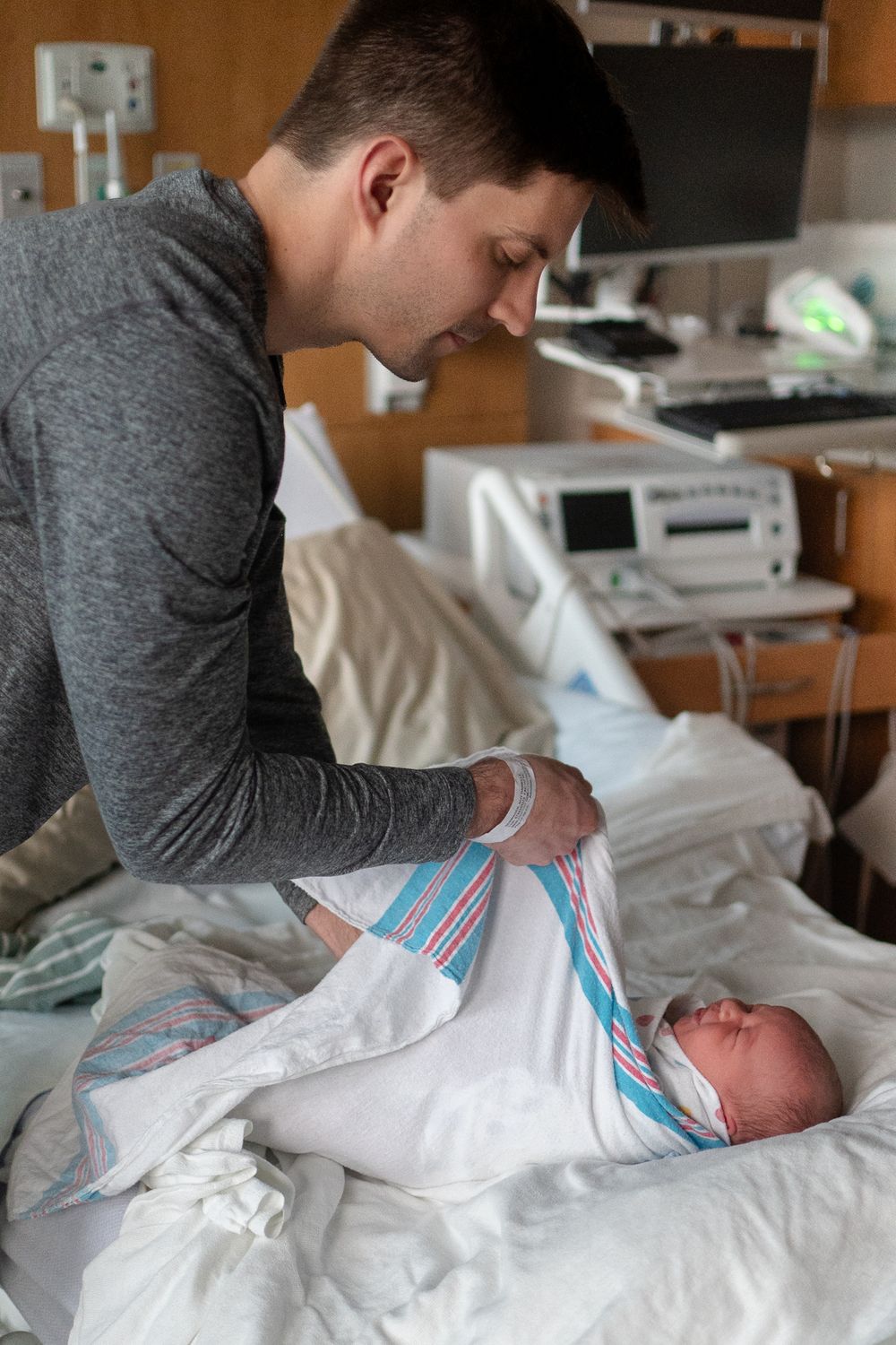 A newborn baby wrapped in hospital blanket is being cared for in a medical setting while wearing a blue and white striped cap.