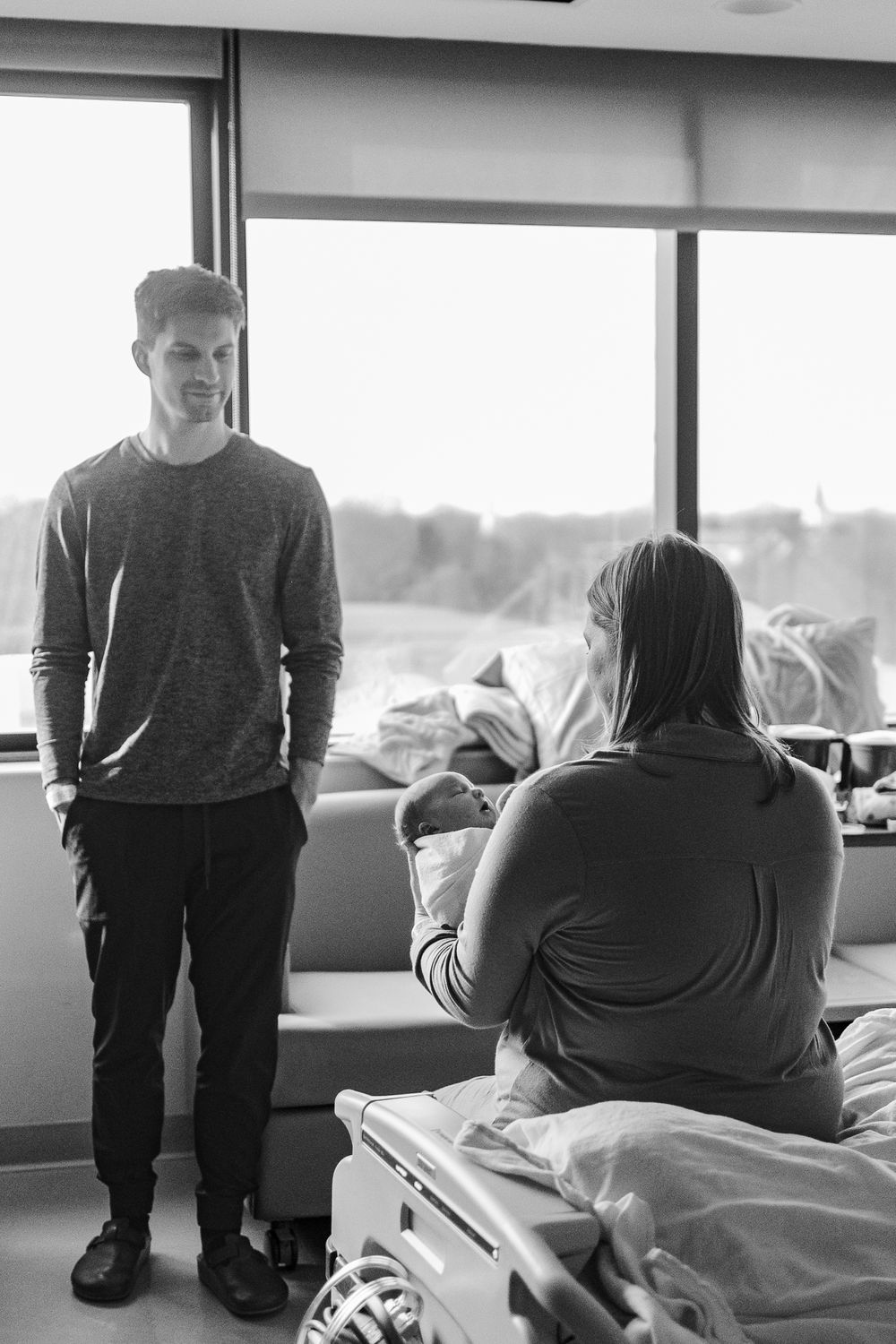 Black and white photo of people in a hospital room with large windows and natural light streaming in.