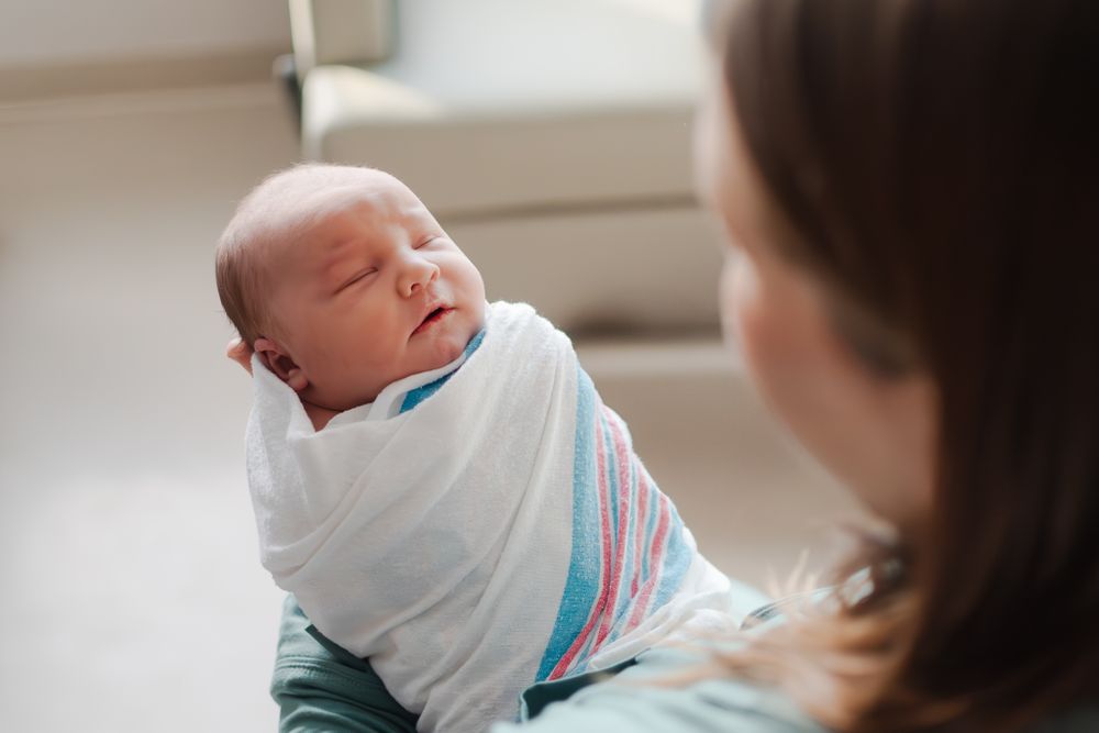 A swaddled newborn baby sleeps peacefully while being cradled in the caregiver's arms.