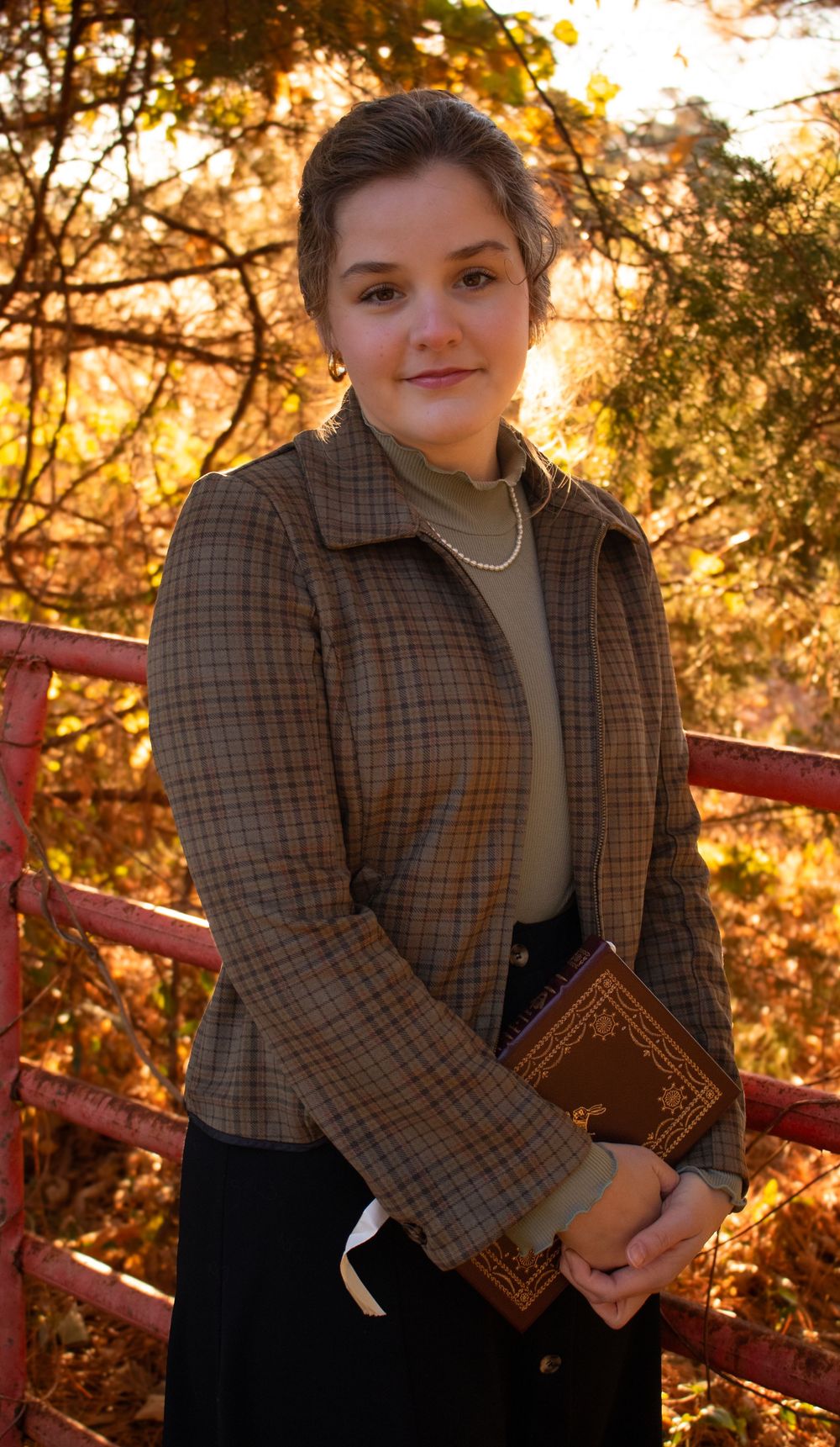 A person in a plaid blazer holds a book while sitting on a red bench during golden hour sunset.