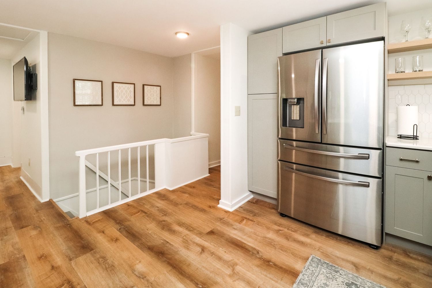 Bright hallway with stainless French door refrigerator, gray cabinets, and light hardwood flooring.