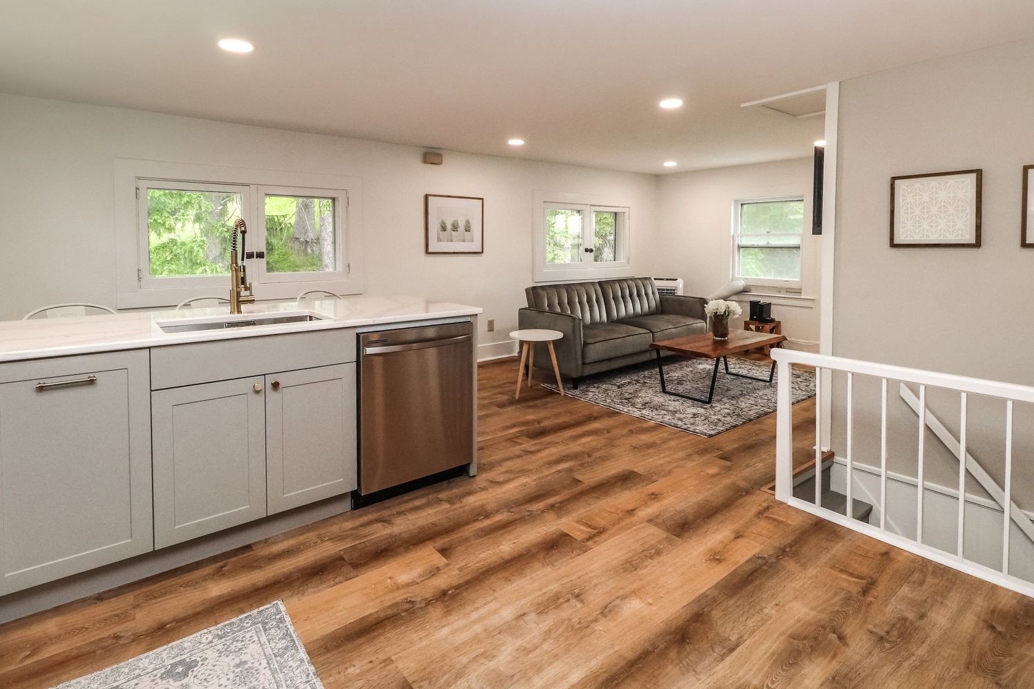 Modern open-plan kitchen with gray cabinets, stainless steel dishwasher, and hardwood floors.