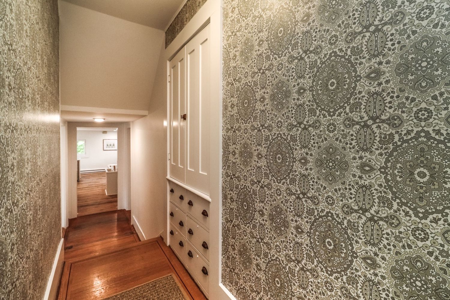 Elegant hallway with intricate patterned wallpaper, white built-in cabinet, and gleaming hardwood floors.