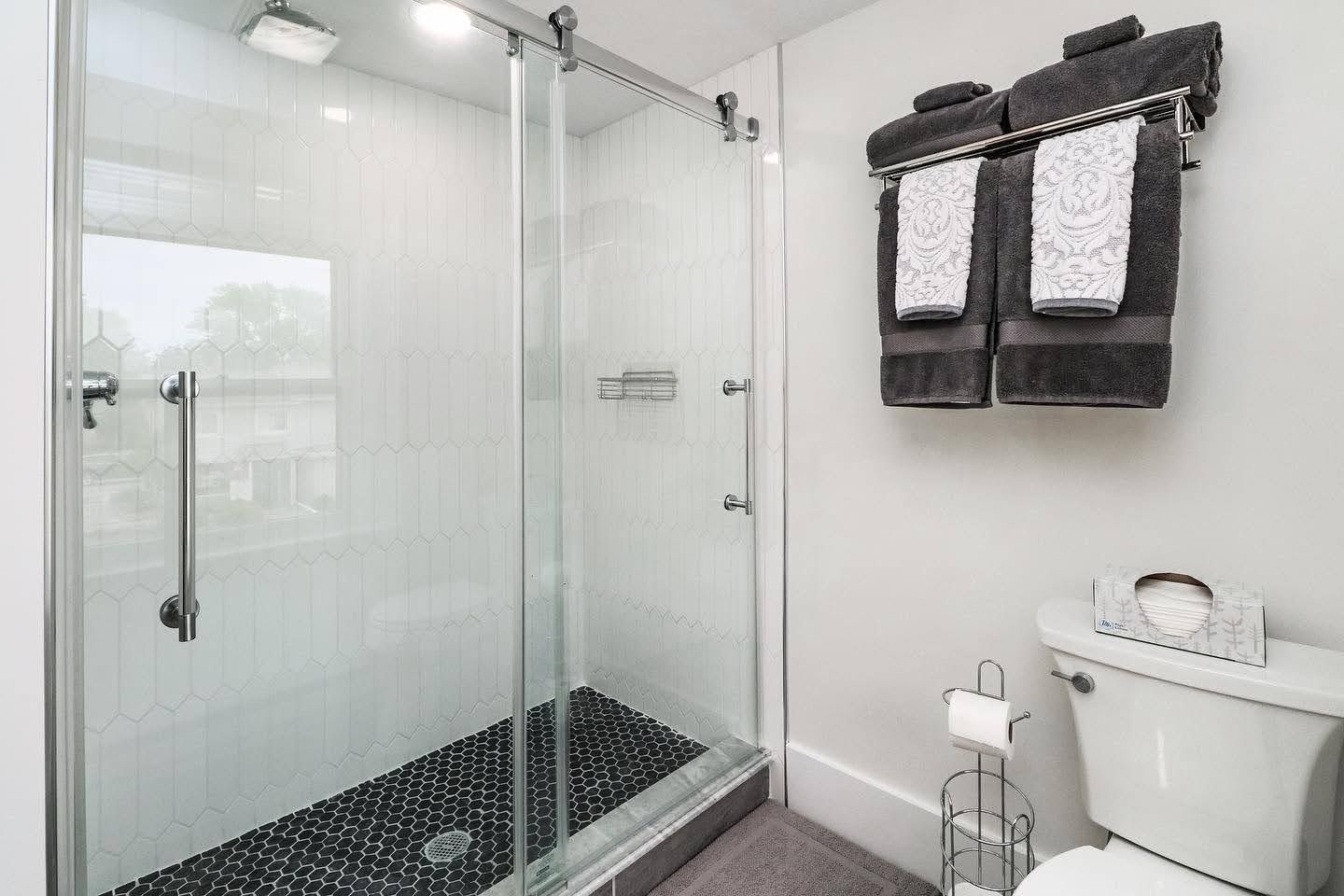Clean white bathroom with glass enclosed shower, black mosaic tile floor, and dark towels.