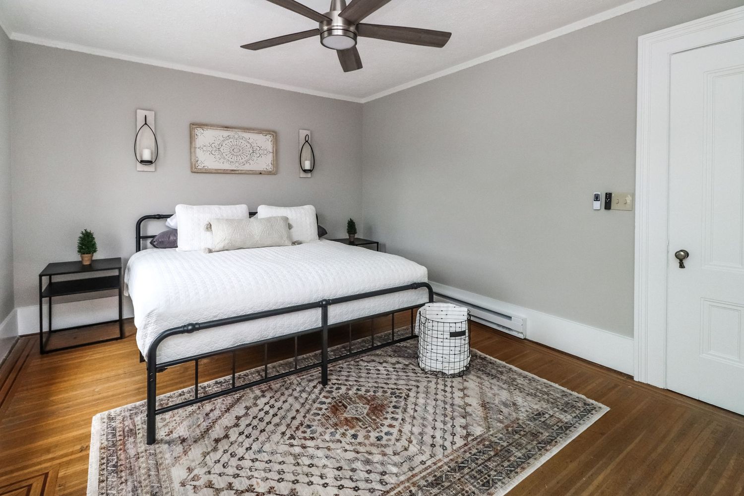 Bright bedroom with black metal bed frame, patterned area rug, hardwood floors, and gray walls.