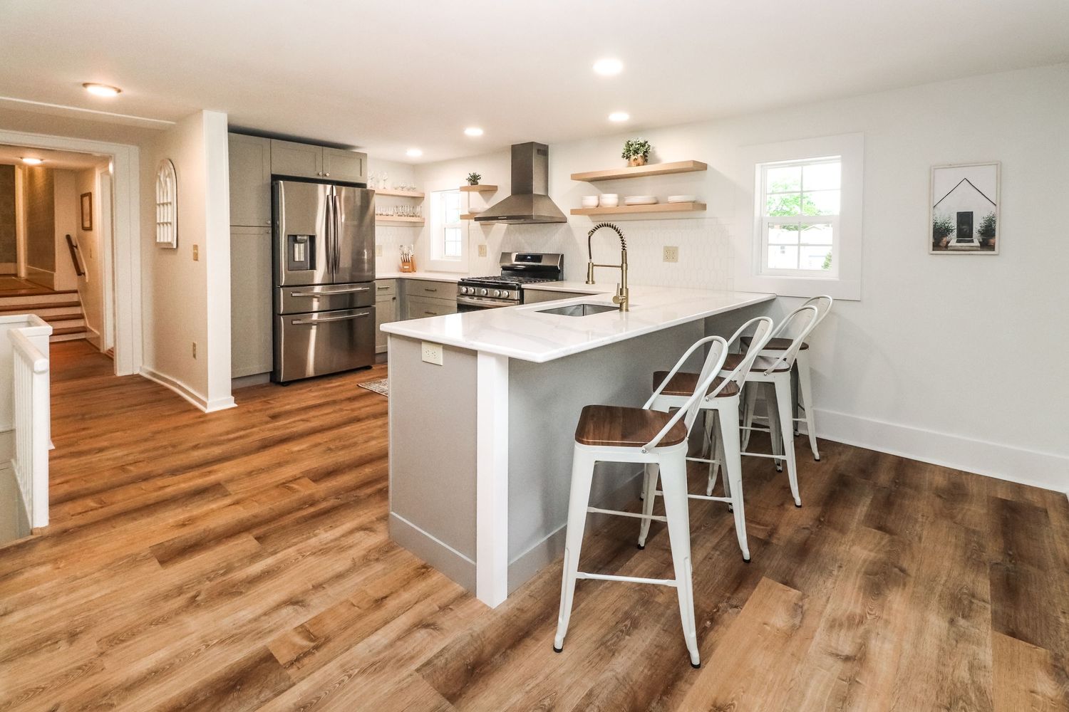 Renovated kitchen with gray island, white countertops, stainless appliances, open shelving, and hardwood floors.