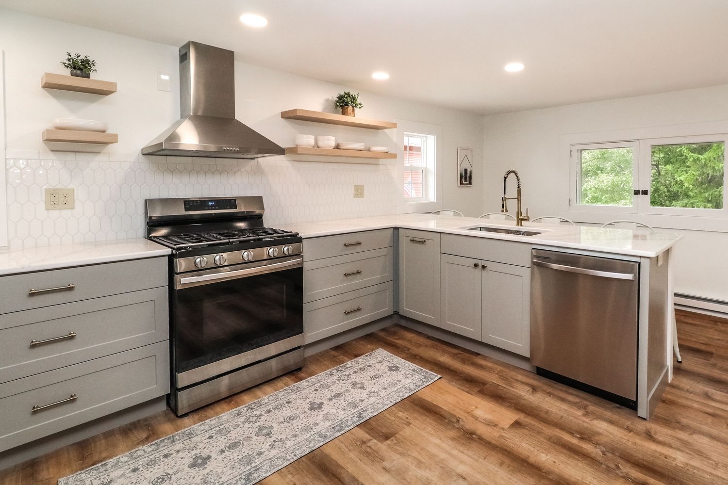 Modern kitchen with gray cabinets, stainless range hood, subway tile backsplash, and hardwood floors.