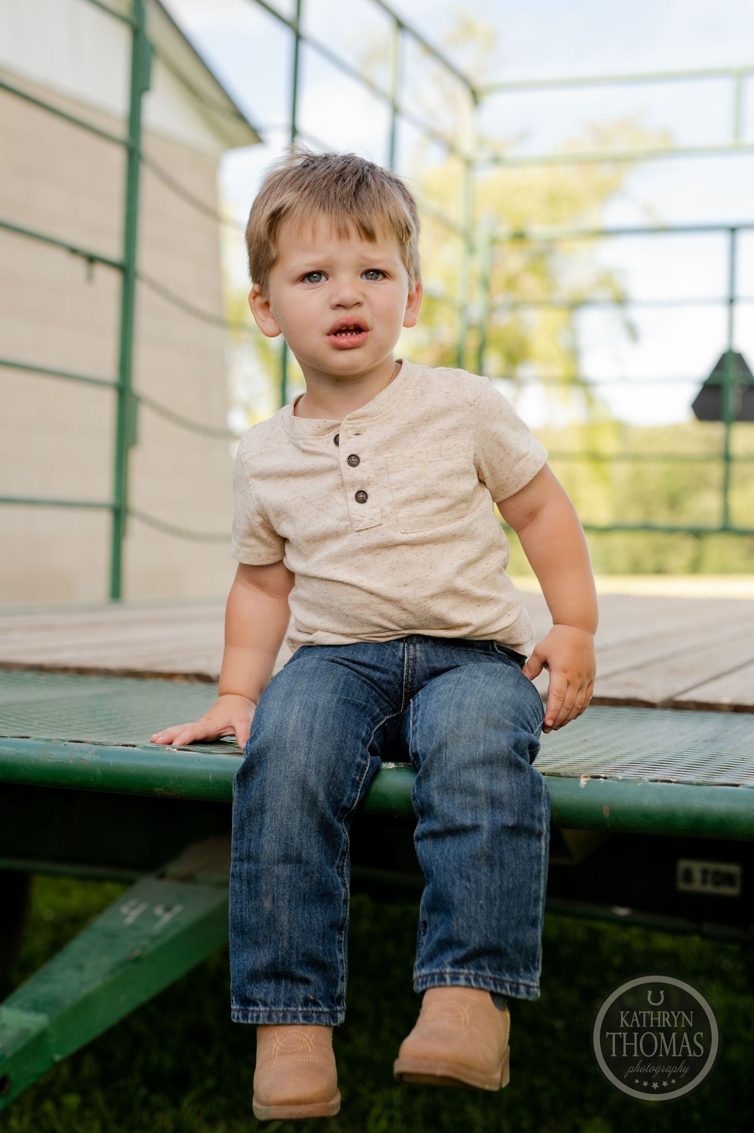 Young child in beige shirt sits on green metal platform outdoors.