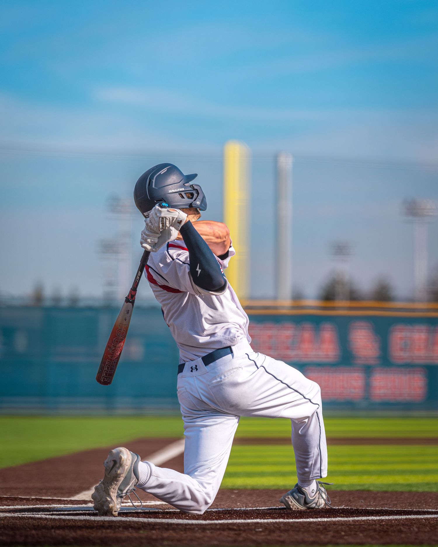 Baseball player in white uniform swings the bat during a game on a sunny day at the ballpark.