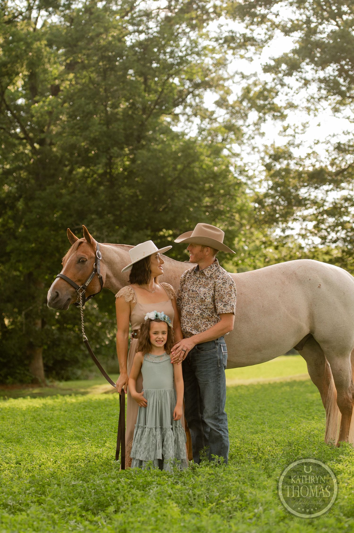 A family group poses with their light-colored horse in a grassy field during golden hour.