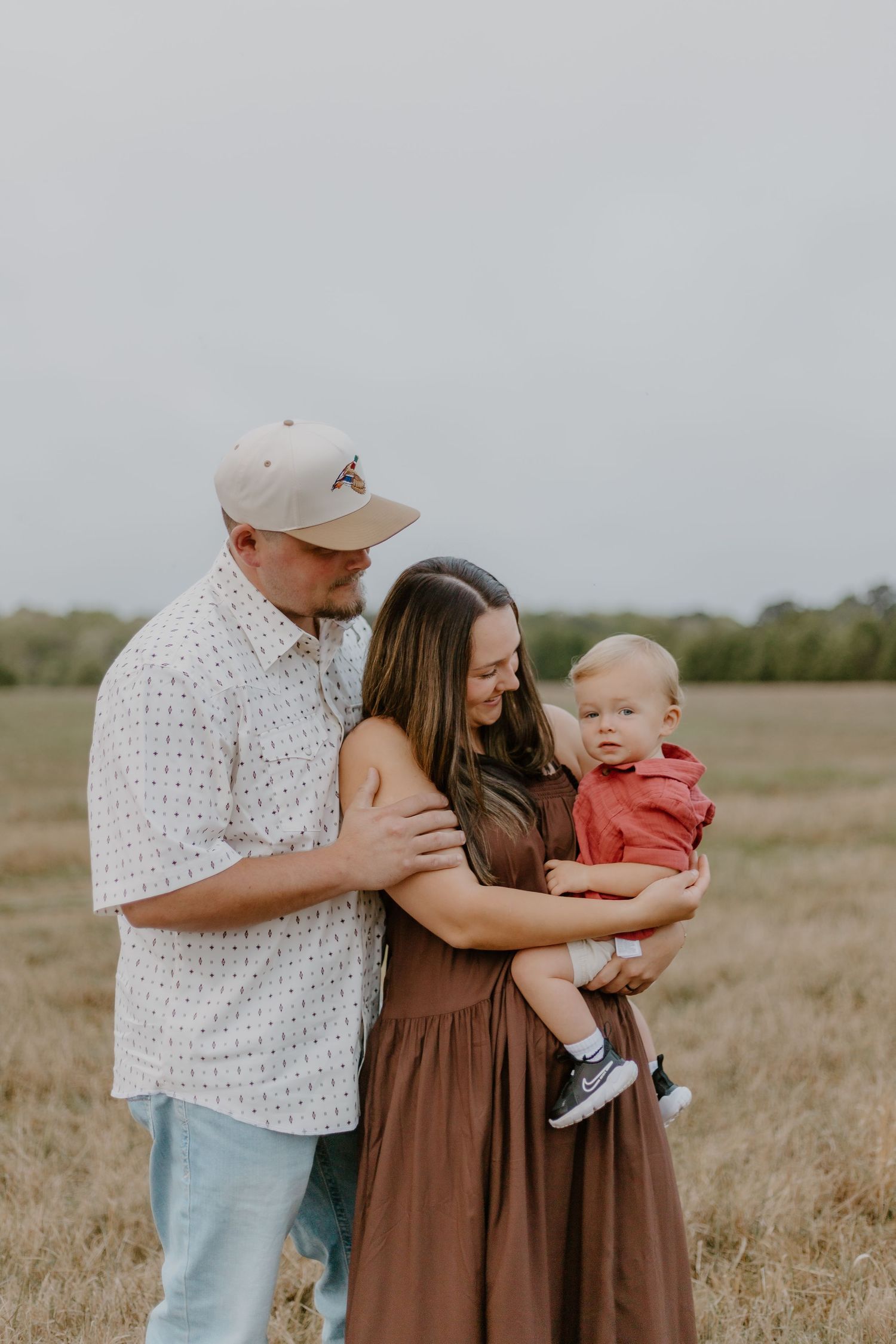 A family enjoys a tender outdoor moment together on a grassy hillside at sunset in autumn.