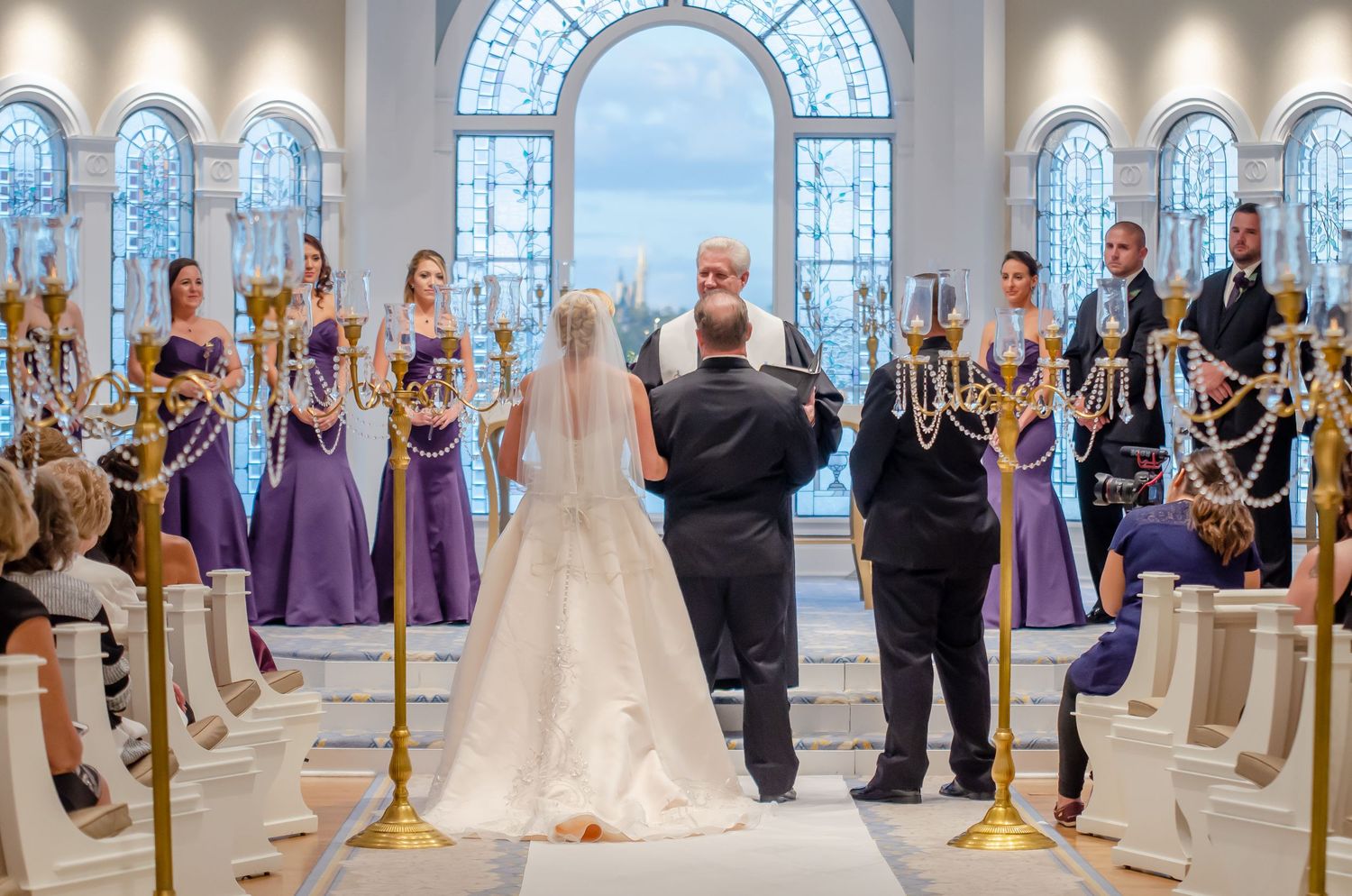 Wedding ceremony with bride and groom at altar, bridesmaids in purple dresses, groomsmen, and guests in elegant chapel.