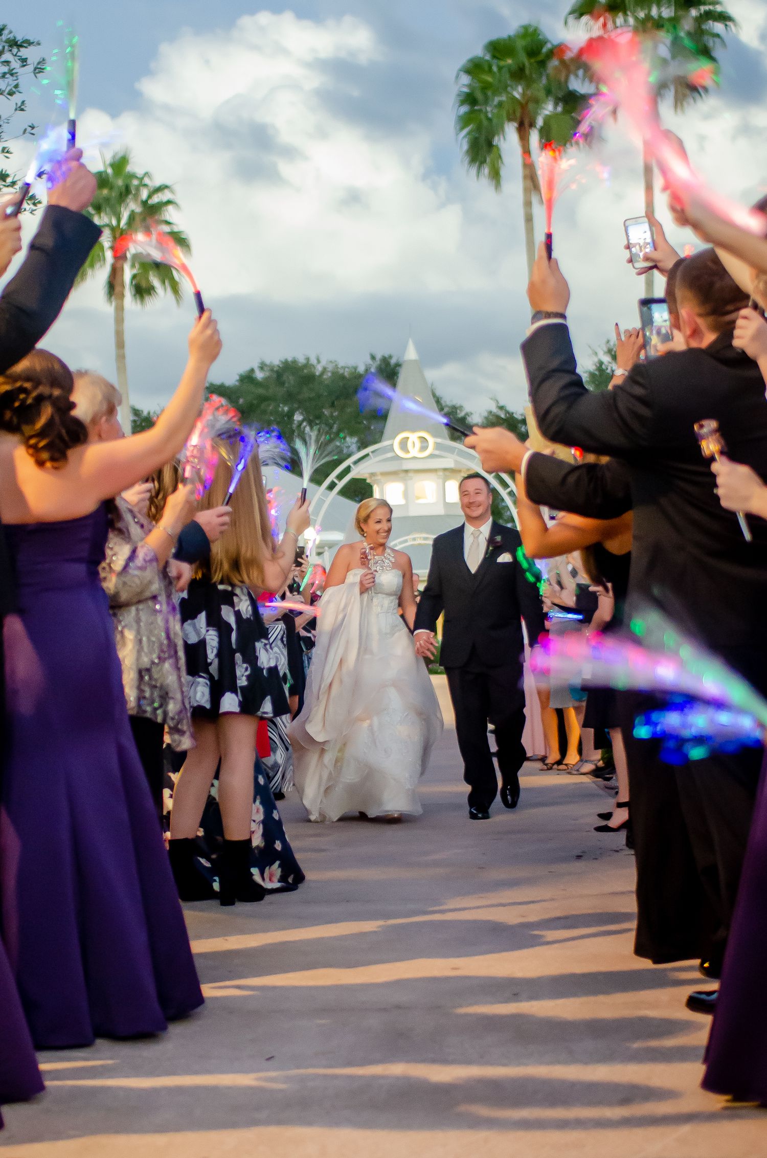 Bride and groom walk through a glowing lightsaber send-off tunnel with guests in purple dresses at a Disney wedding.