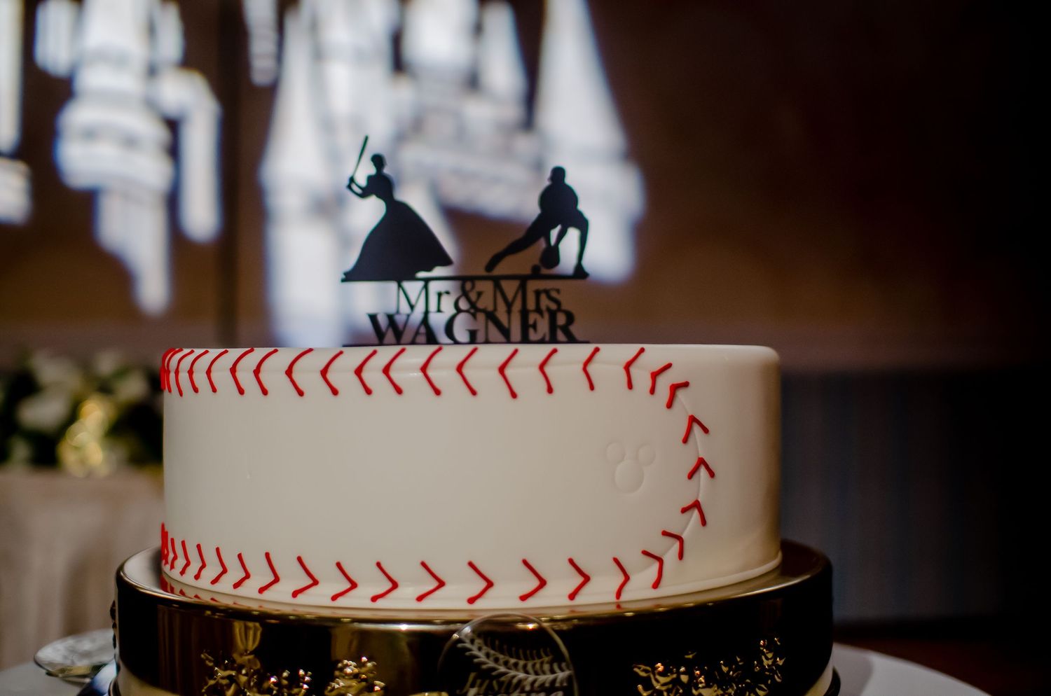 Baseball-themed wedding cake with red stitching and Wagner name topper featuring bride and groom silhouettes.