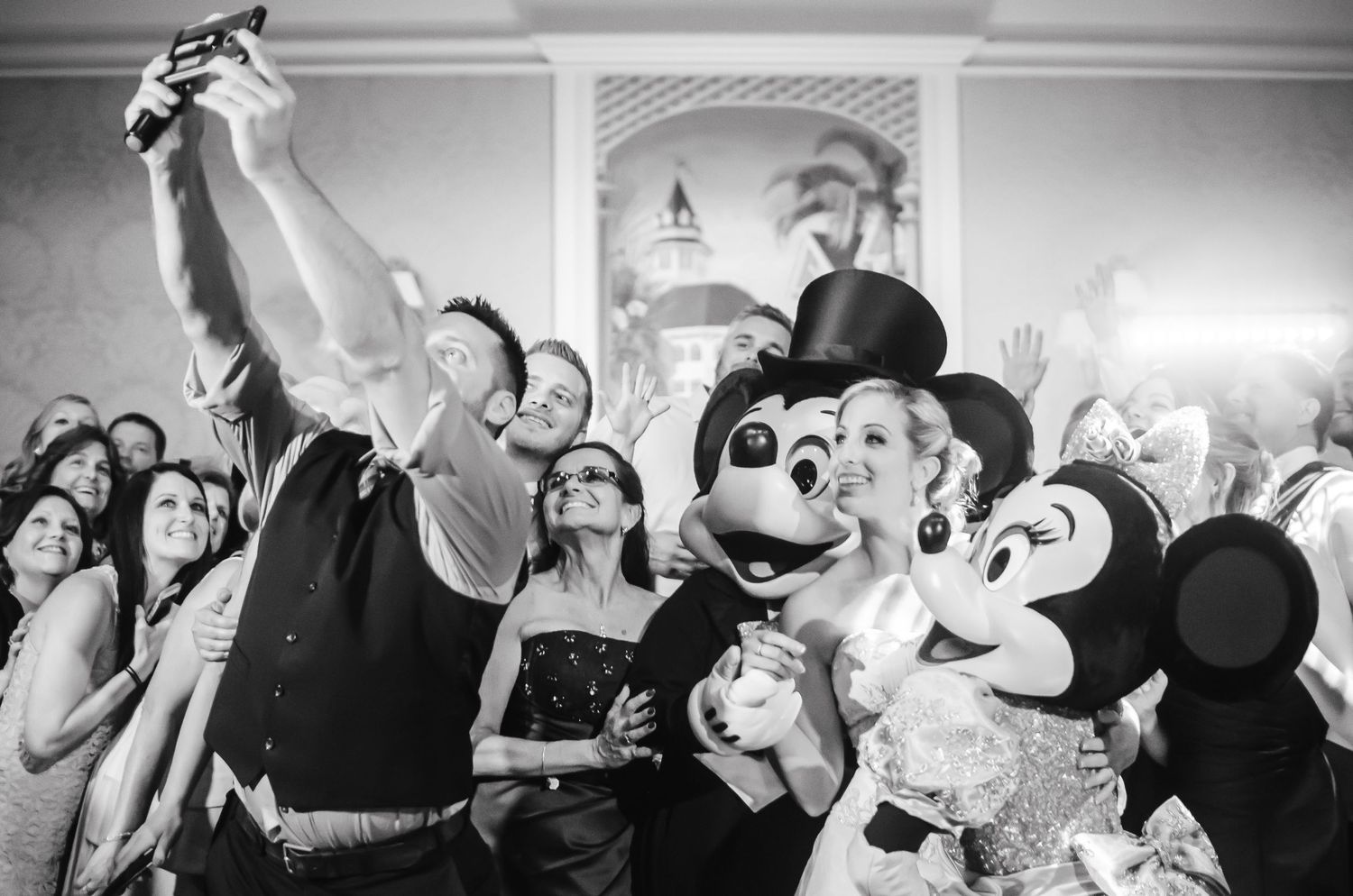 Wedding guests take a fun selfie with Mickey and Minnie Mouse characters at a lively Disney-themed wedding reception.