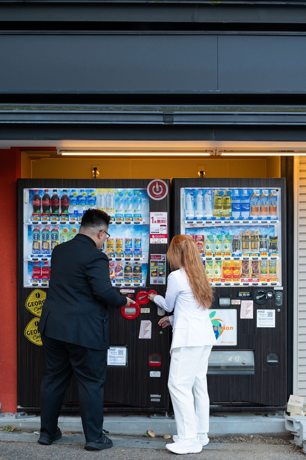 Couple using a Japanese vending machine together, man in black suit and woman in white outfit.