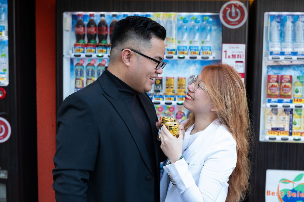 Smiling couple sharing a snack in front of a colorful Japanese vending machine.