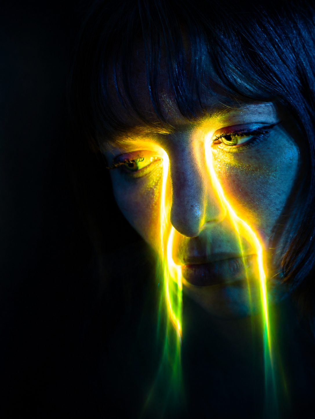 A woman's face illuminated by glowing yellow and green light streaks in a dark, dramatic portrait.