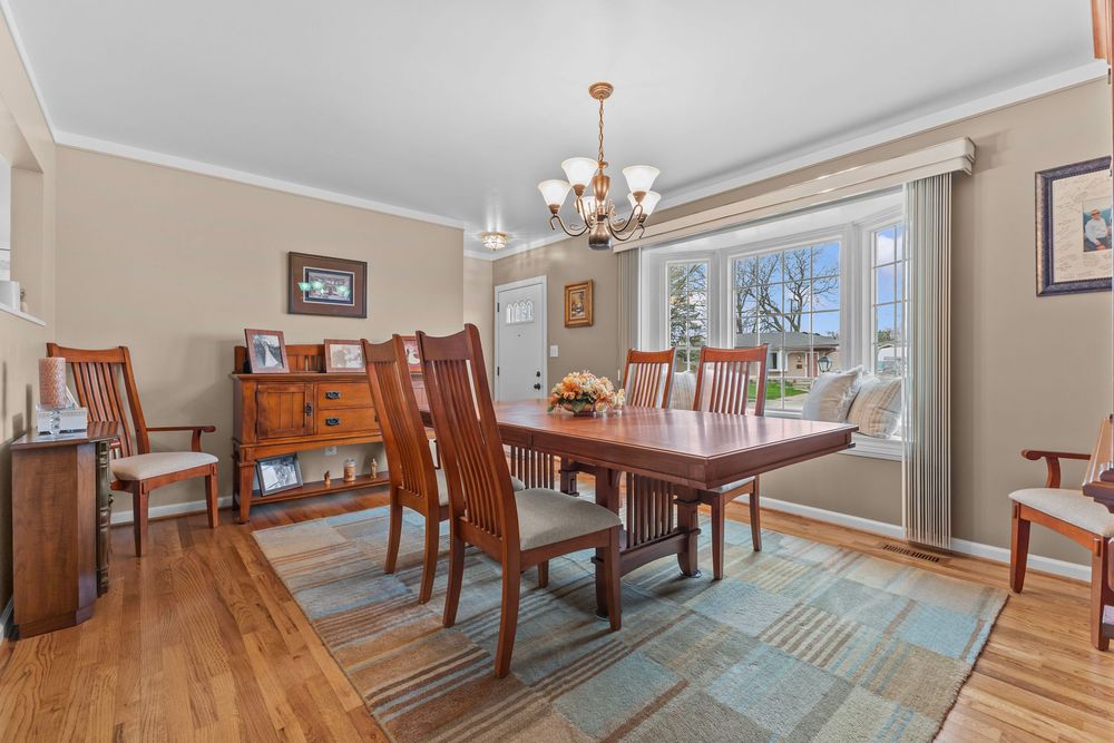 Elegant dining room with cherry wood table and chairs, hardwood floors, crown molding, and a chandelier near a bright window.